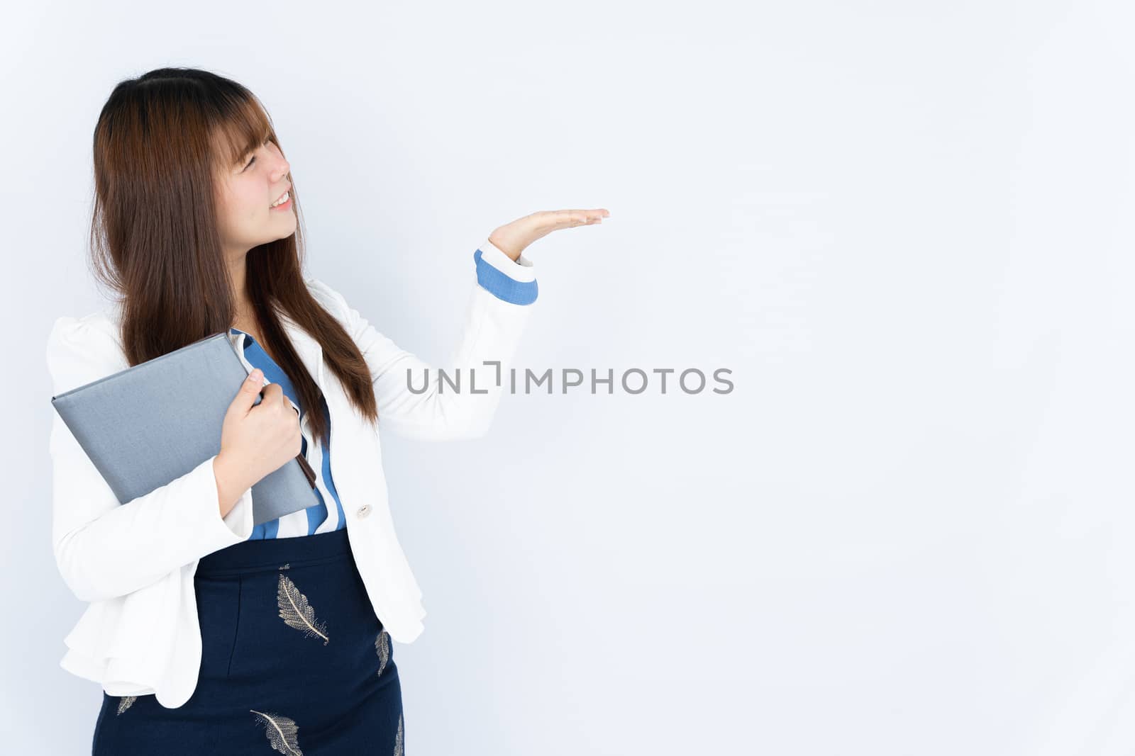 Smiling Asian business woman wearing a medical face mask holding the notebook and pointing hand to side blank space over grey background. Back to the normal concept.Smiling Asian business woman holding the notebook and pointing hand to side blank space over grey background. Back to the normal concept. by mikesaran