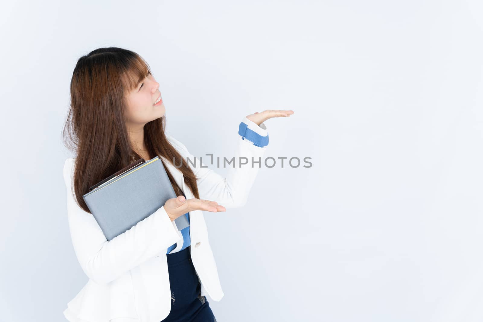 Smiling Asian business woman holding the notebook and pointing hand to side blank space over grey background. Back to the normal concept.