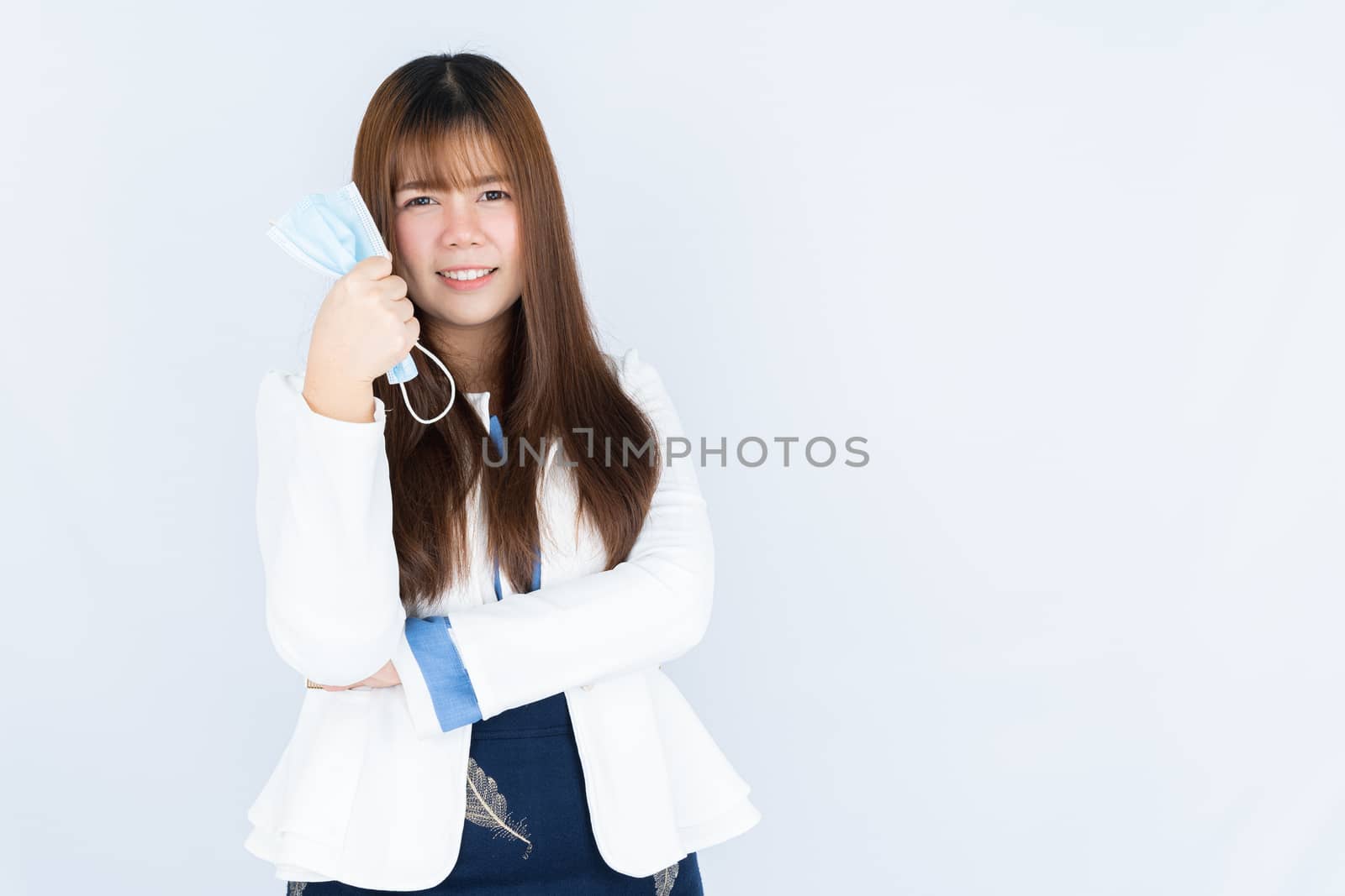 Smiling Asian business woman shows hand grasping mask over grey background. Back to the normal concept. by mikesaran