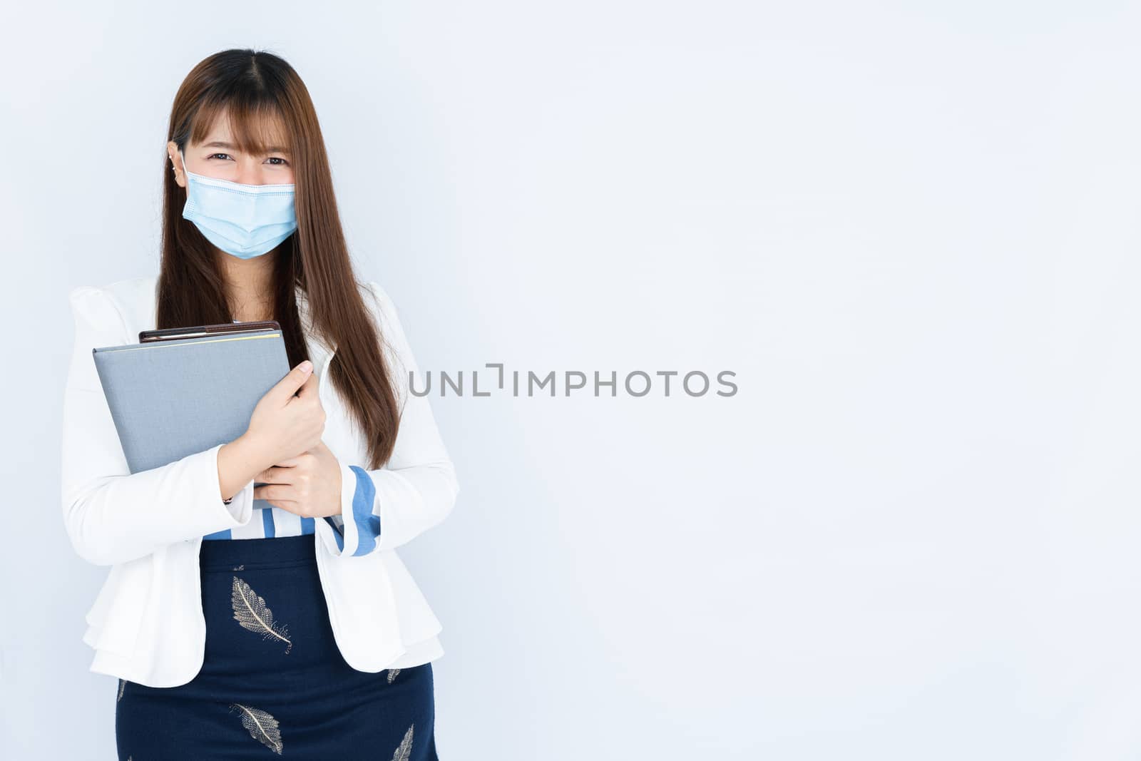 Smiling Asian business woman holding the notebook and looking at the camera over grey background. Back to the normal concept.