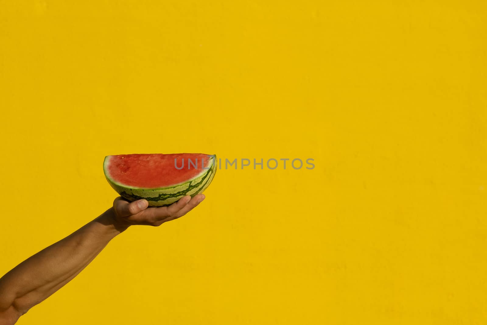 A man's hand holding a piece of watermelon on a yellow background. Diet, summer, slimming concept
