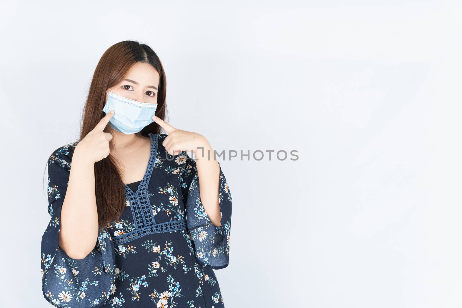 Asian beautiful happy hipster woman wearing a medical protection face mask for protect the coronavirus, filter dust PM 2.5 and cold and her finger point on her mask on white background