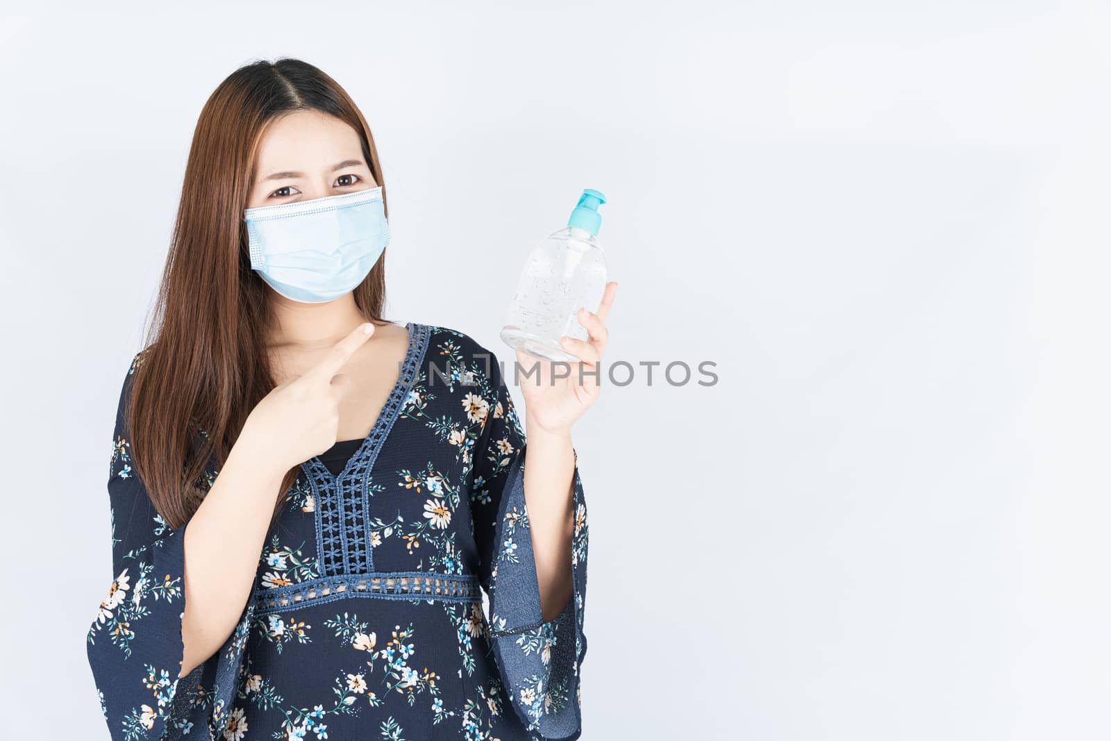 Asian beautiful happy hipster woman wearing a medical protection face mask for protect the coronavirus, filter dust PM 2.5 and cold and finger pointing to sanitizer hand gel on white background