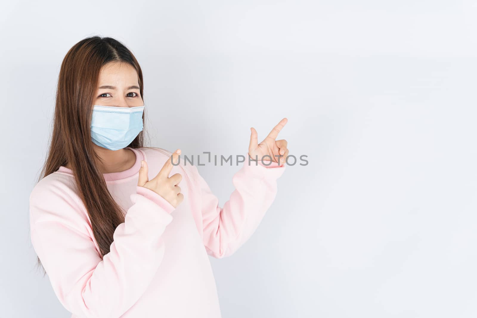 Asian beautiful happy hipster woman wearing a medical protection face mask for protect the coronavirus, filter dust PM 2.5 and cold and her finger pointing outside on the white background