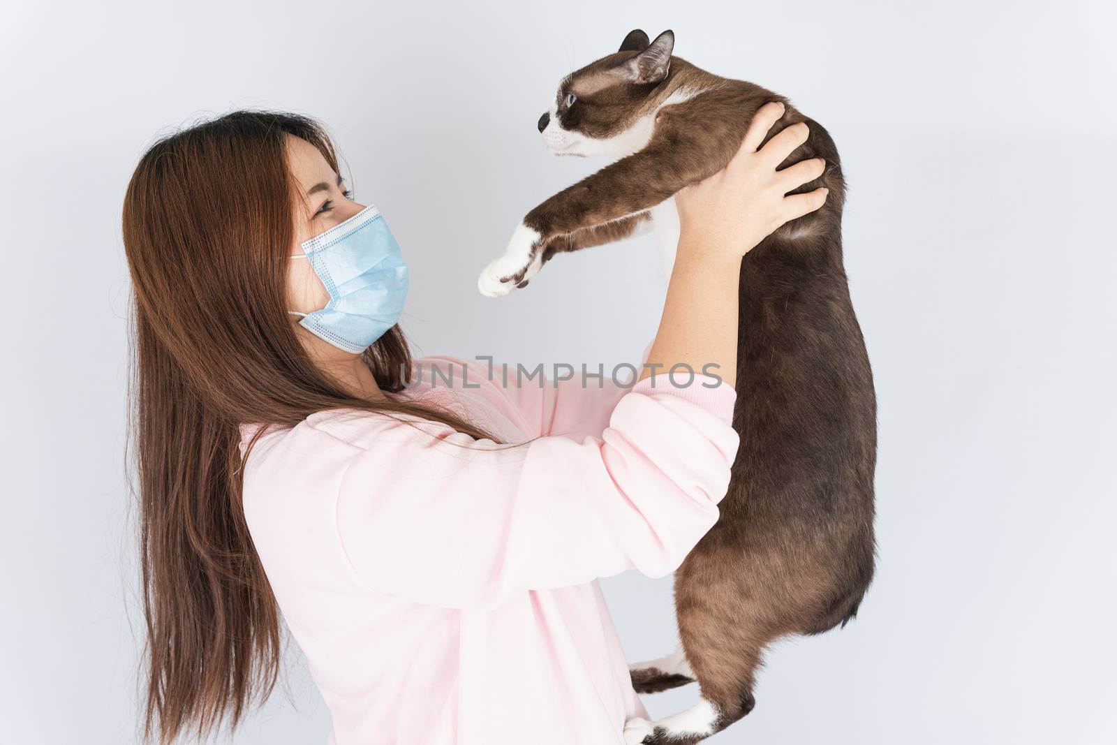 Asian beautiful happy woman wearing a medical protection face mask for protect the coronavirus, filter dust PM 2.5, cold and allergic to cat fur and she carry a cat on the white background