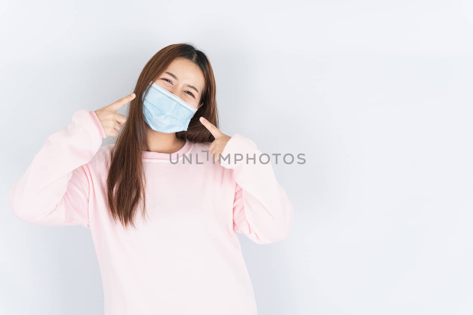Asian beautiful happy hipster woman wearing a medical protection face mask for protect the coronavirus, filter dust PM 2.5 and cold and her finger point on her mask on white background