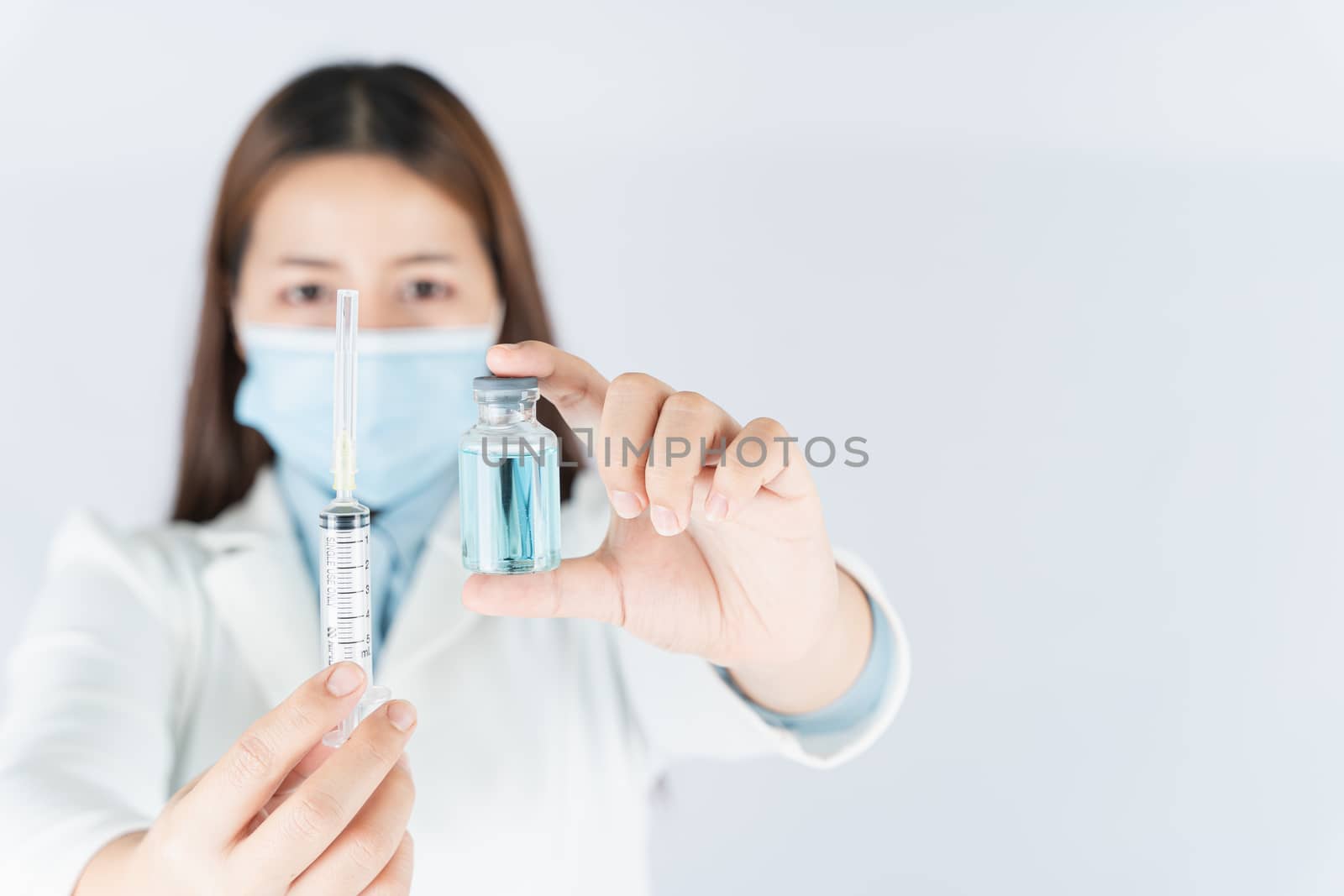 Closeup hand of woman doctor or scientist wearing medical mask and holding syringe and medicine liquid vaccine vial bottle. COVID 19 or coronavirus concept.
