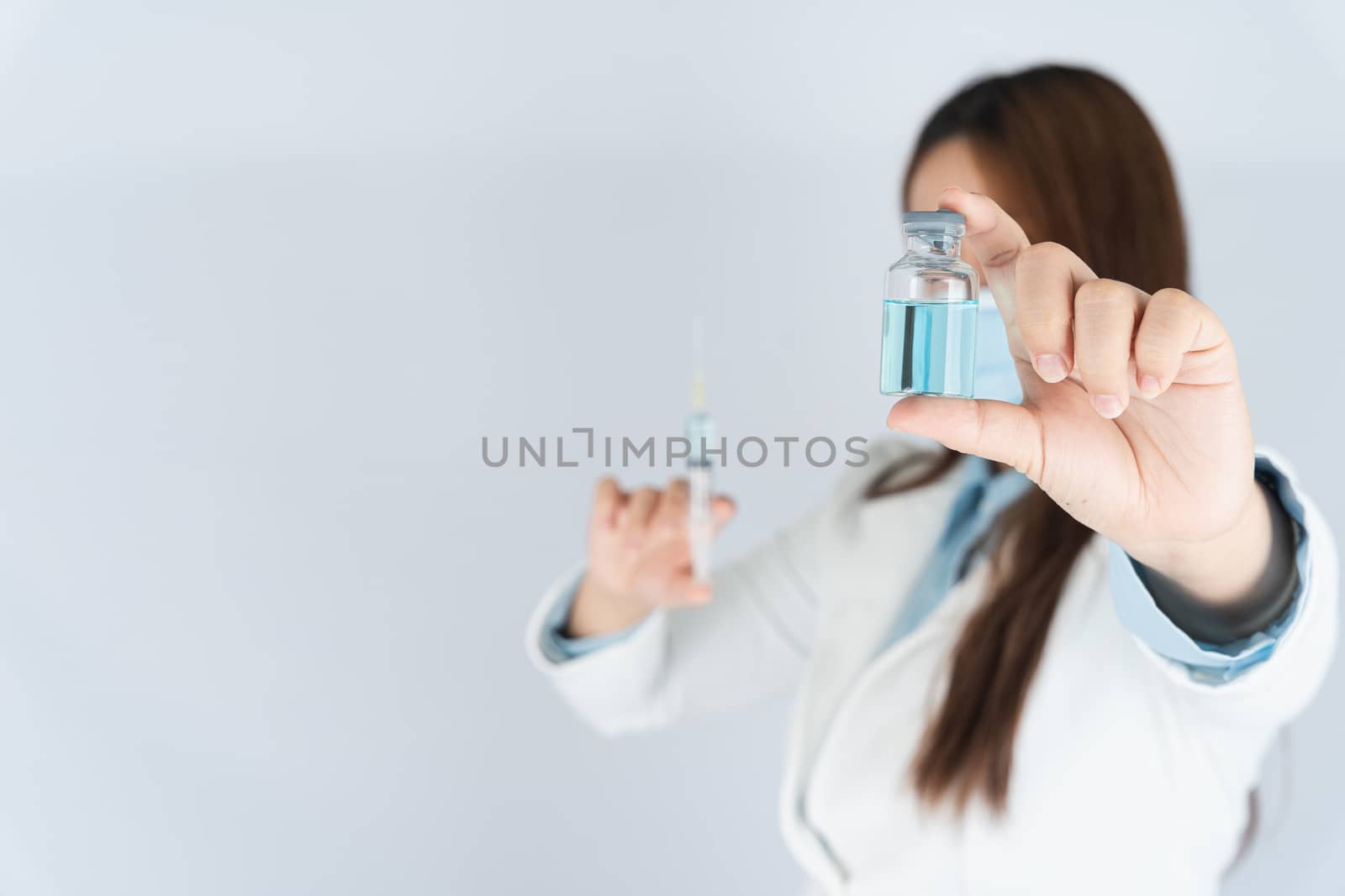 Closeup hand of woman doctor or scientist wearing medical mask and holding syringe and medicine liquid vaccine vial bottle. COVID 19 or coronavirus concept.