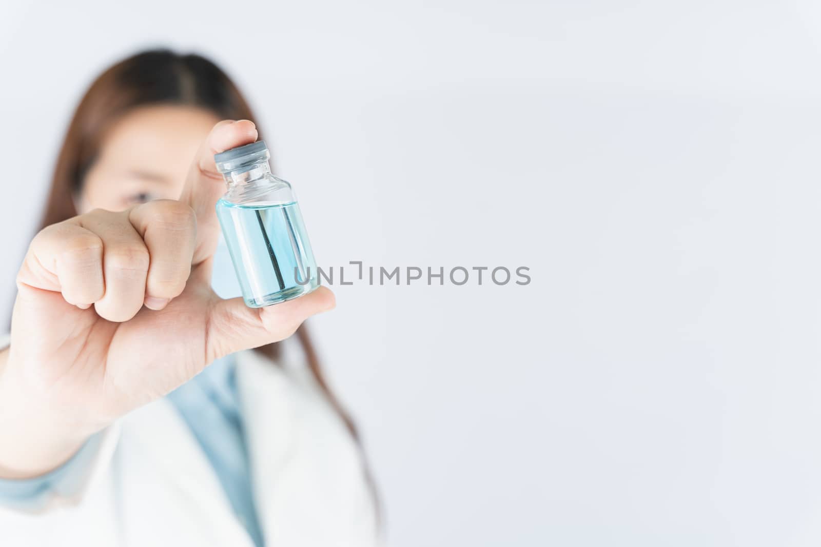 Closeup hand of woman doctor or scientist wearing medical mask and holding medicine liquid vaccine vial bottle. COVID 19 or coronavirus concept.