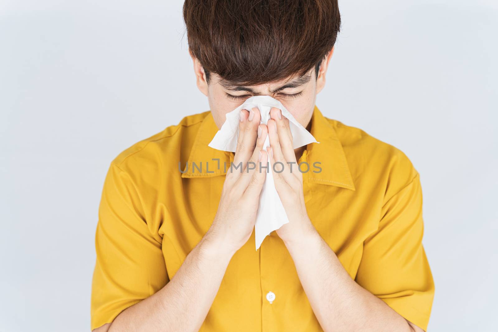 Asian handsome happy hipster man blowing a nose to tissue paper from the coronavirus, dust PM 2.5 and cold on white background