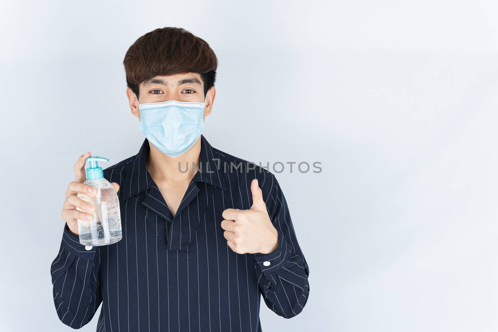 Asian handsome happy hipster man wearing a medical protection face mask for protect the coronavirus, filter dust PM 2.5 and cold and showing sanitizer hand gel and thumbs up on white background