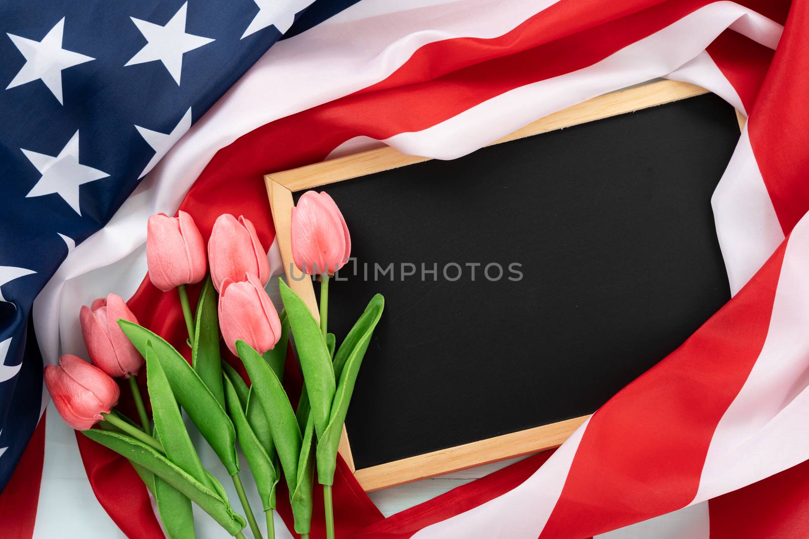 US American flag with blackboard and tulip flower on blue wooden background. For USA Memorial day, Presidents day, Veterans day, Labor day, Independence or 4th of July celebration. Top view, copy space for text.