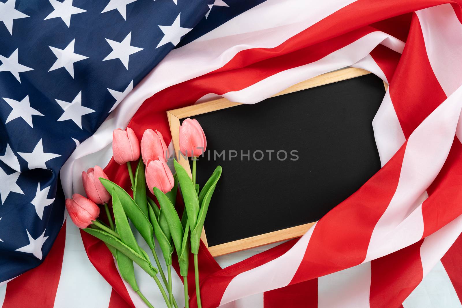 US American flag with blackboard and tulip flower on blue wooden background. For USA Memorial day, Presidents day, Veterans day, Labor day, Independence or 4th of July celebration. Top view, copy space for text.