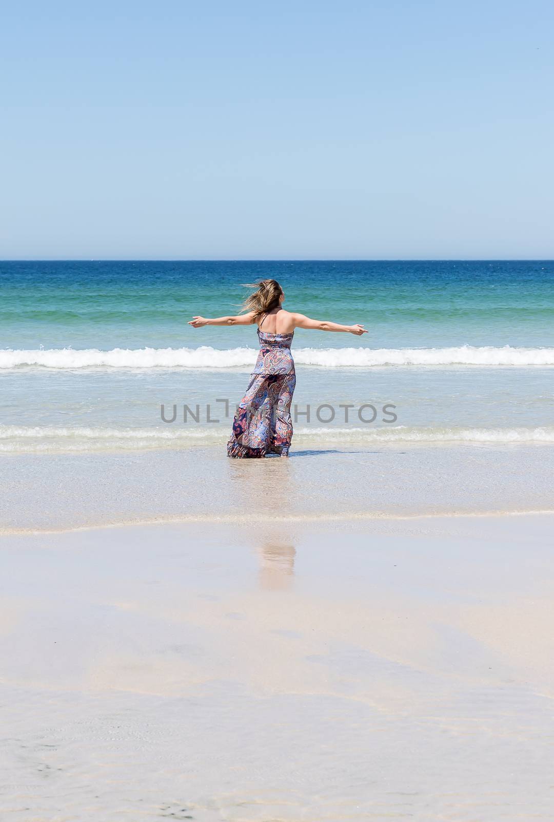 Middle-aged blonde woman relaxing at the beach with arms open enjoying her freedom facing the sea