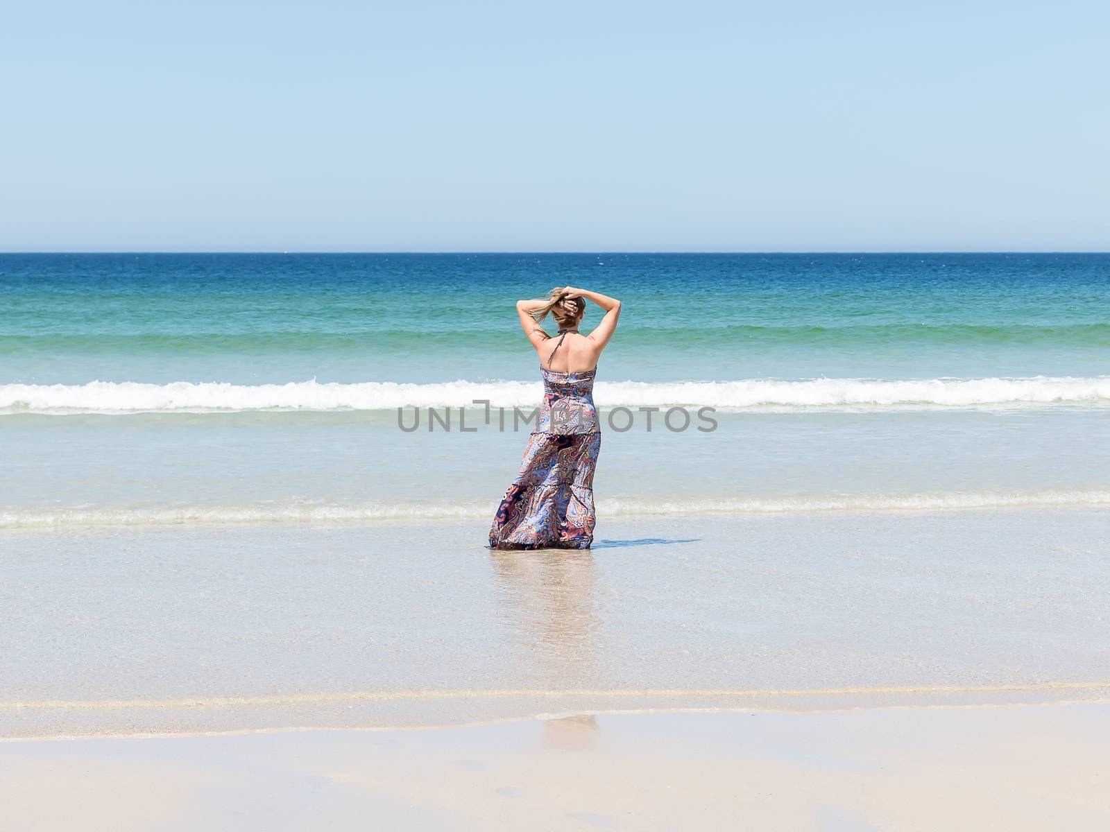 Woman relaxing on the beach with her hands on the back of her head enjoying her freedom facing the sea