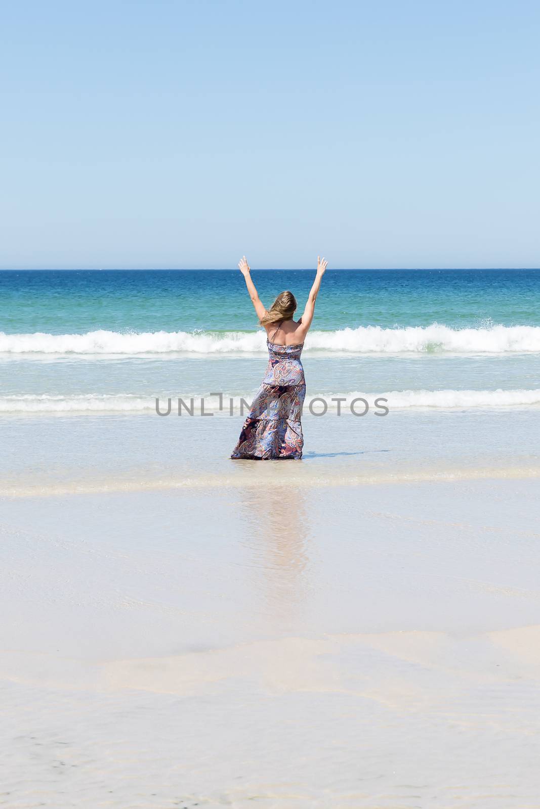 Middle-aged blonde woman relaxing at the beach with arms open enjoying her freedom facing the sea