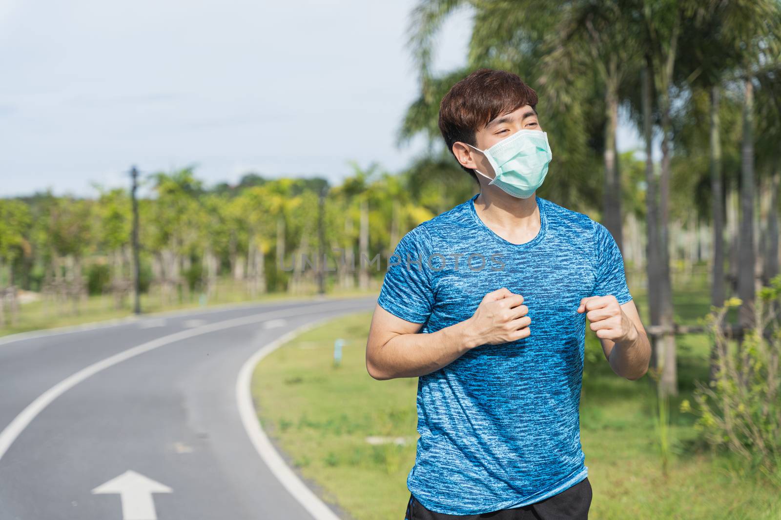 Young male wearing medical mask while running workout session at the park. Stay in fit during quarantine in the days of the Corona Virus or Covid-19