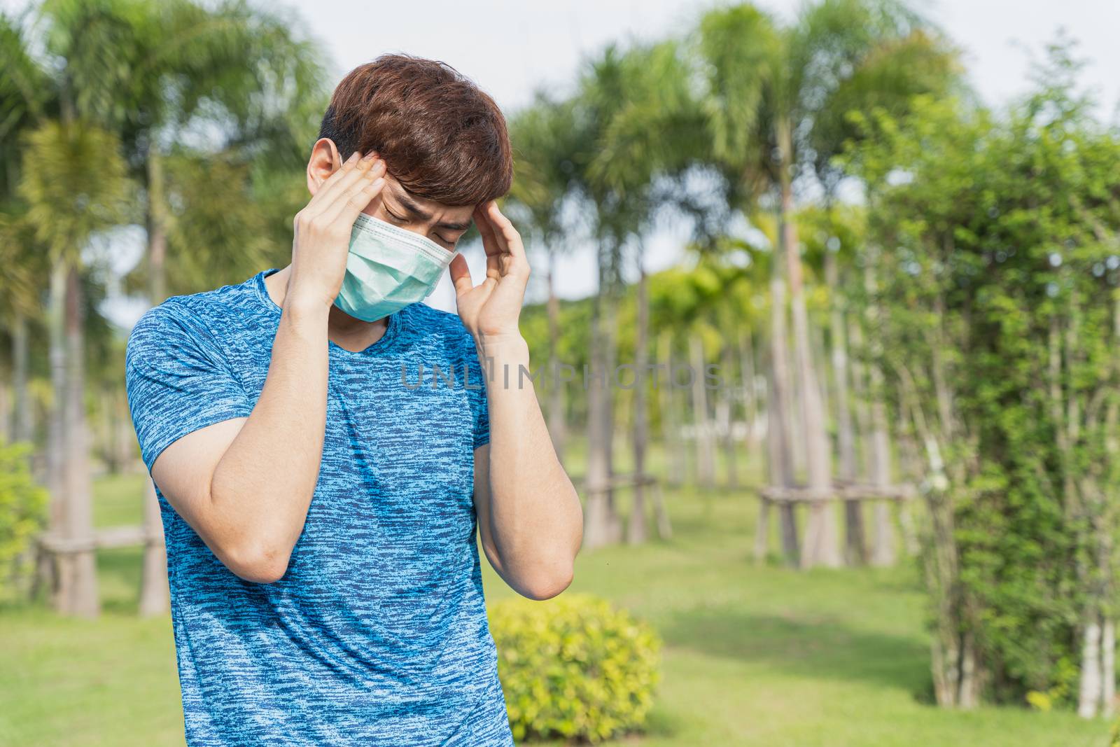 Young male wearing medical mask have headache while workout at the park. Stay in fit during quarantine in the days of the Corona Virus or Covid-19