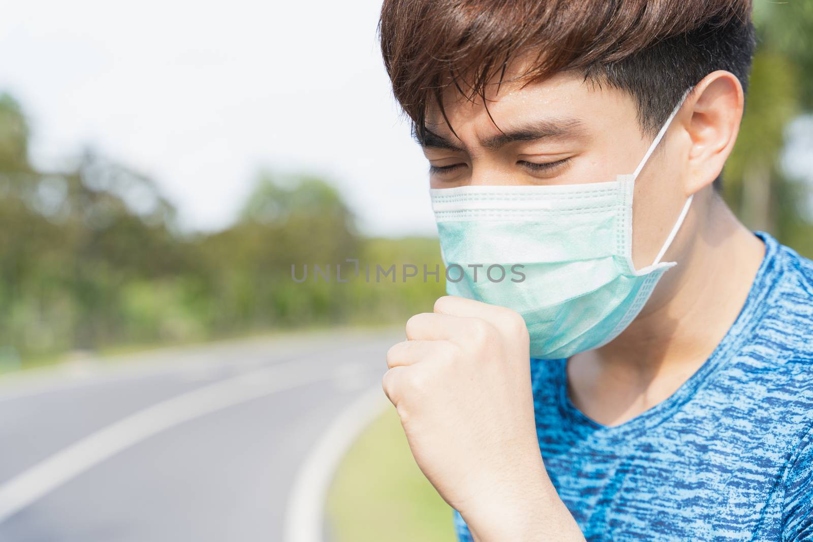Young male wearing medical mask and coughing while workout at the park. Stay in fit during quarantine in the days of the Corona Virus or Covid-19