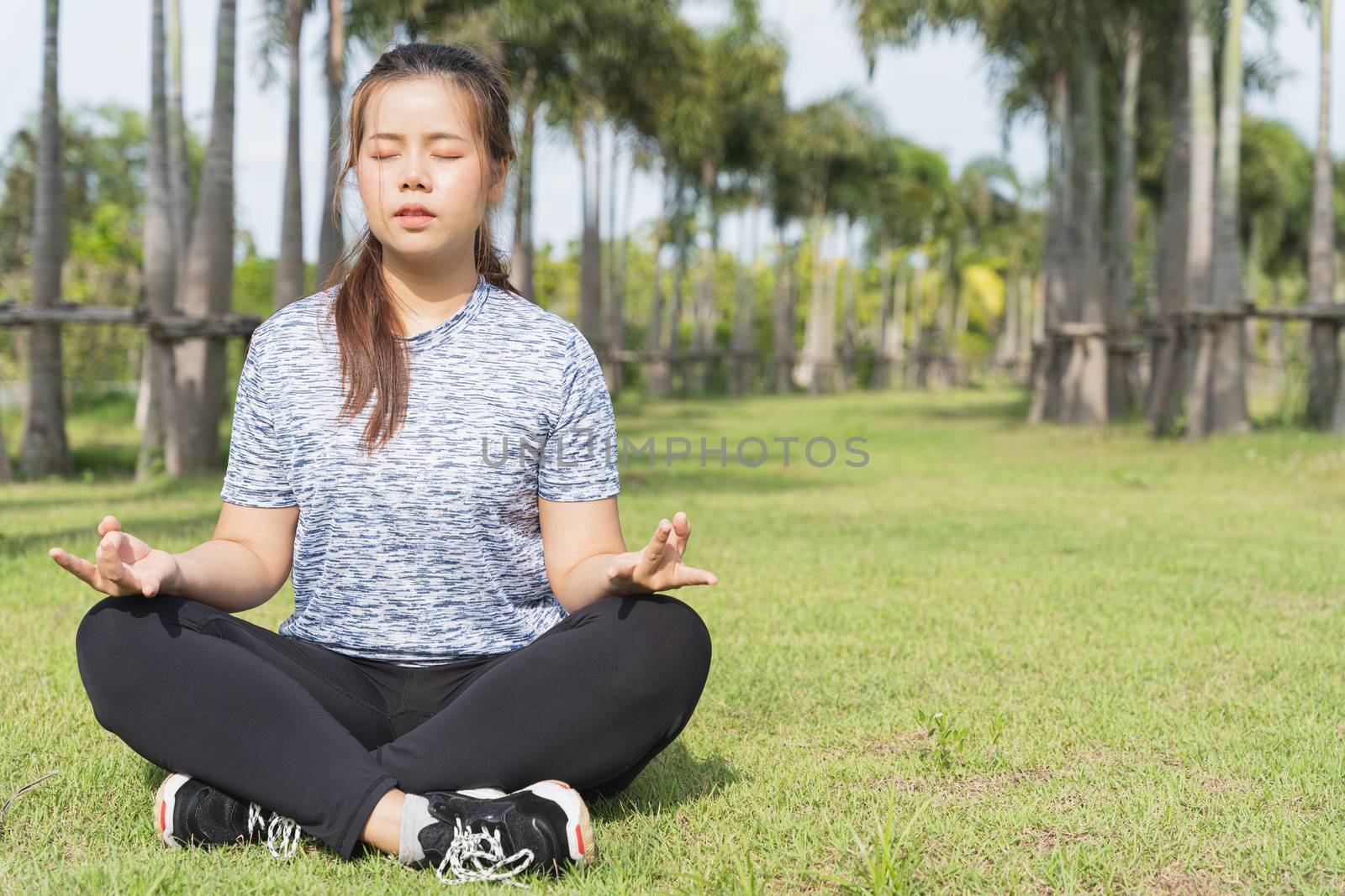 Young woman practicing yoga and meditation in the lotus position in the park.
