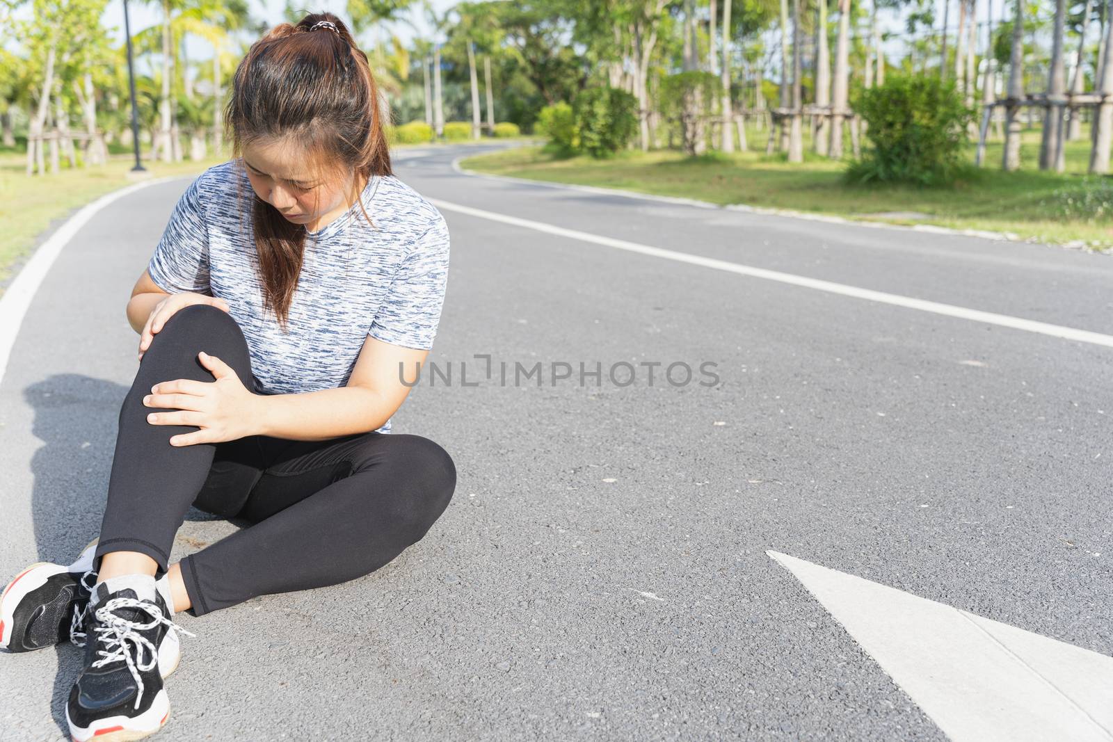 Asian woman use hands hold on her knee injury while running on road in the park, Injury from workout concept.