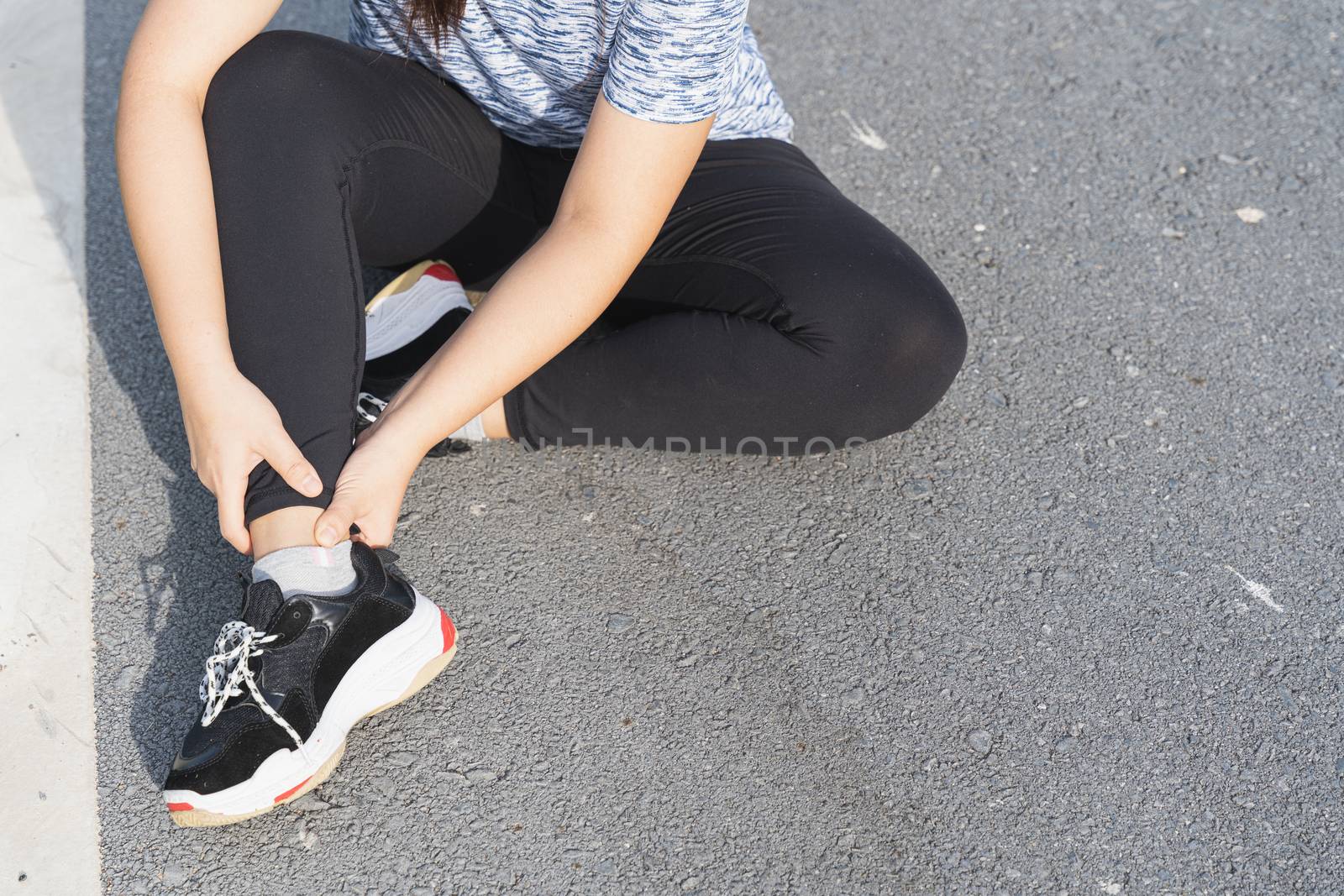 Asian woman use hands hold on her ankle while running on road in the park. Injury from workout concept.