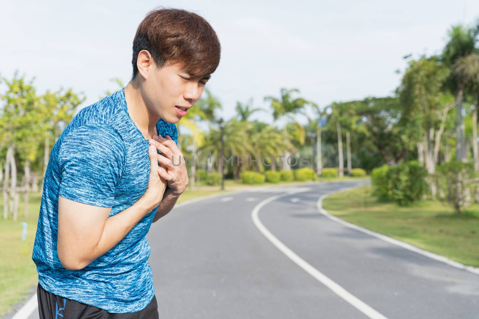 Exhausted male runner suffering painful angina pectoris or asthma breathing problems after running at the park. Sport and healthcare concept.