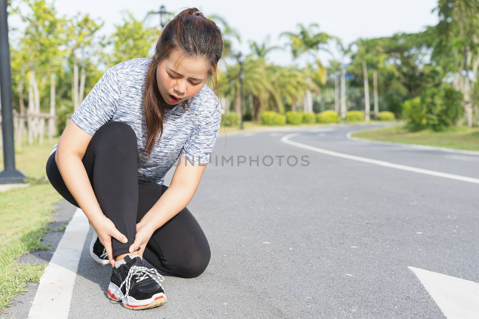 Asian woman use hands hold on her ankle while running on road in the park. Injury from workout concept.