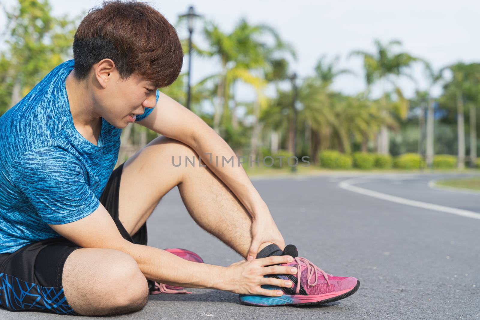 Asian man use hands hold on his ankle while running on road in the park. Injury from workout concept.