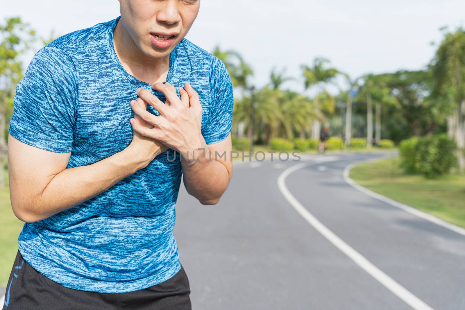 Exhausted male runner suffering painful angina pectoris or asthma breathing problems after running at the park. Sport and healthcare concept.