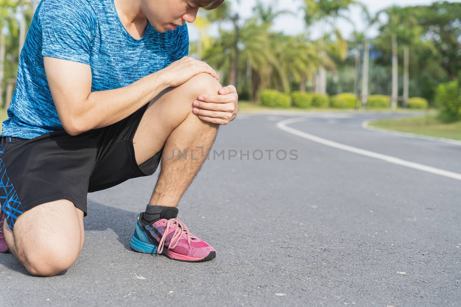 Asian man use hands hold on his knee injury while running on road in the park, Injury from workout concept.