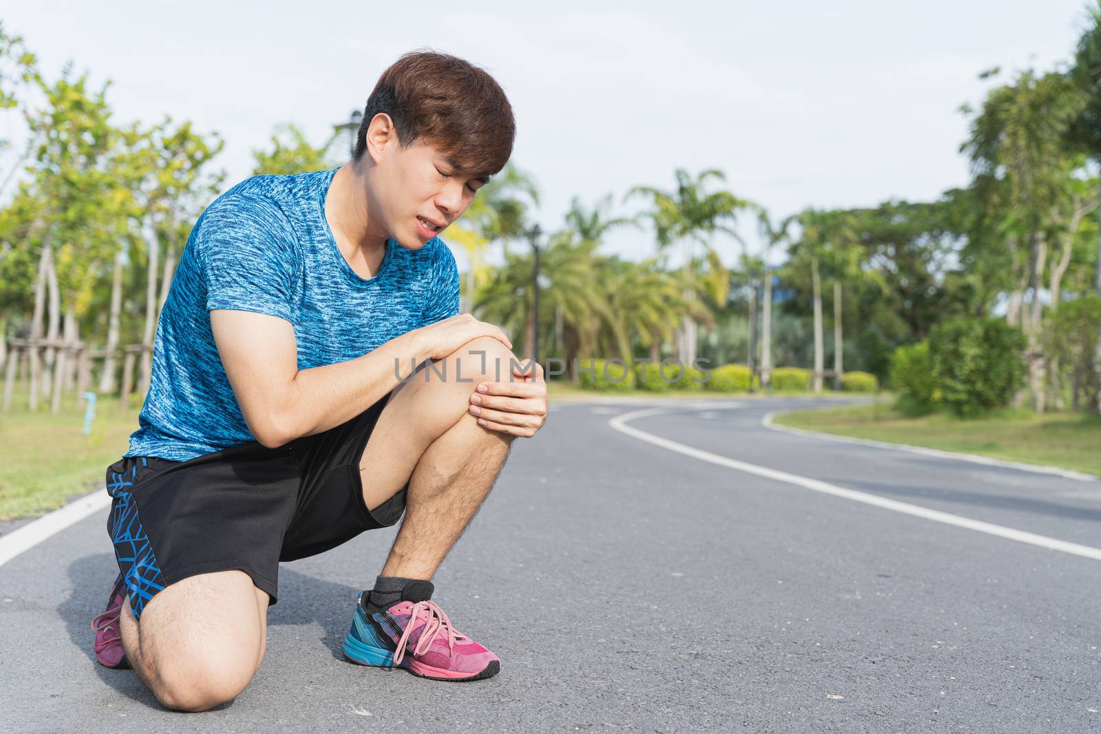 Asian man use hands hold on his knee injury while running on road in the park, Injury from workout concept.