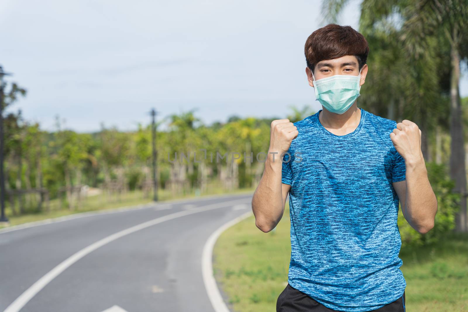 Young male wearing medical mask and show her hand to fight them before workout training session at the park. Stay in fit during quarantine in the days of the Corona Virus or Covid-19
