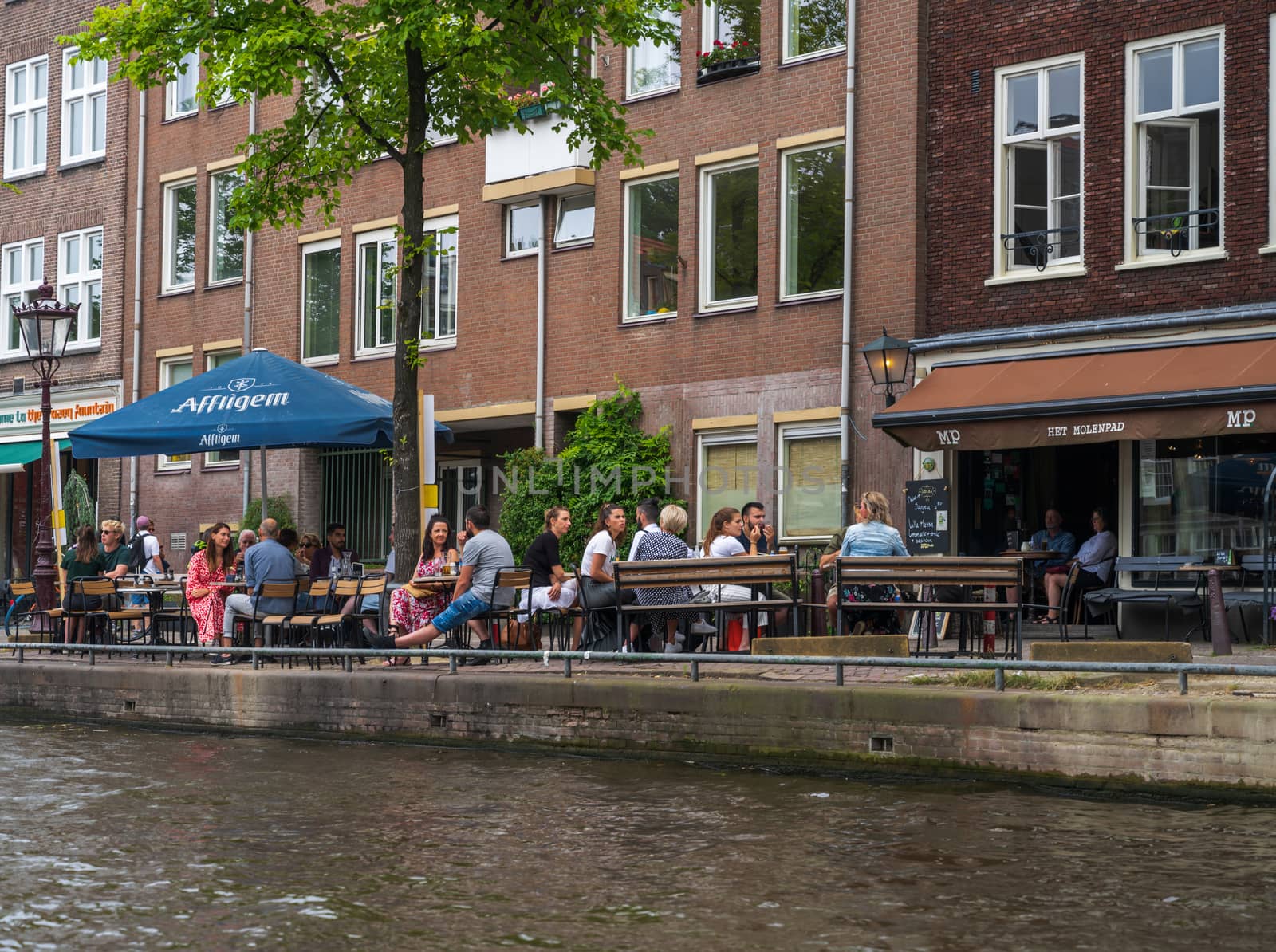 Amsterdam, the Netherlands — July 28, 2019. Groups of people are seated and having refreshments  at an outdoor cafe by an Amsterdam canal.