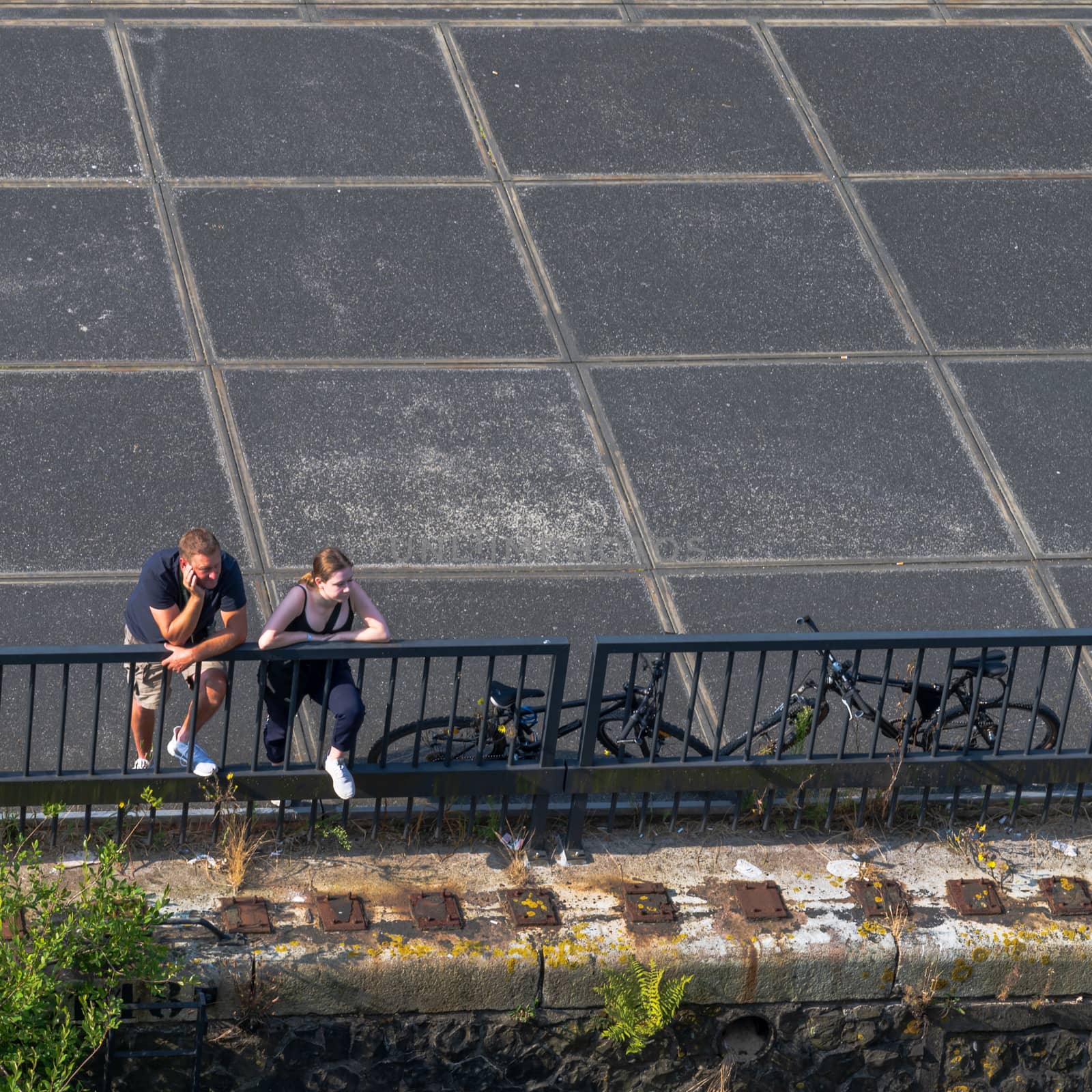 Amsterdam, the Netherlands — July 28, 2019. A photo looking down at a man and a woman leaning on a fence near a pier peering into the distance.