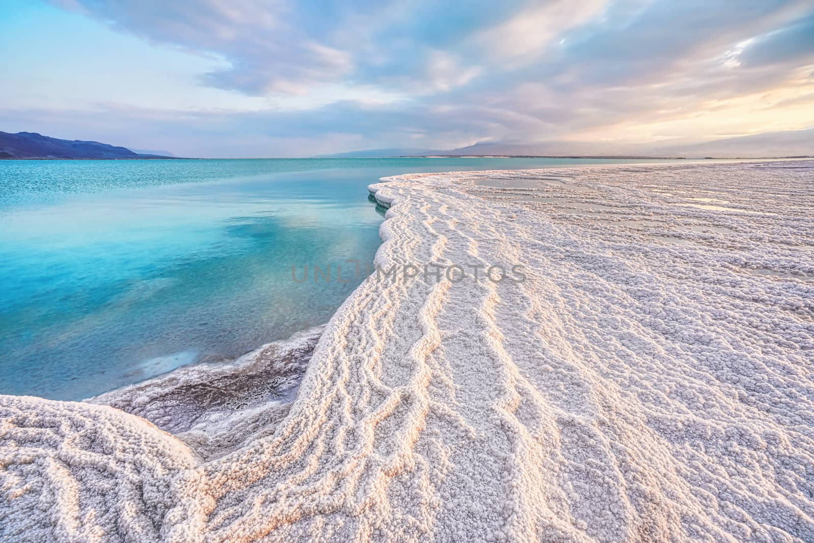 Morning sun shines on salt crystals formations, clear cyan green calm water near, typical landscape at Ein Bokek beach, Israel by Ivanko