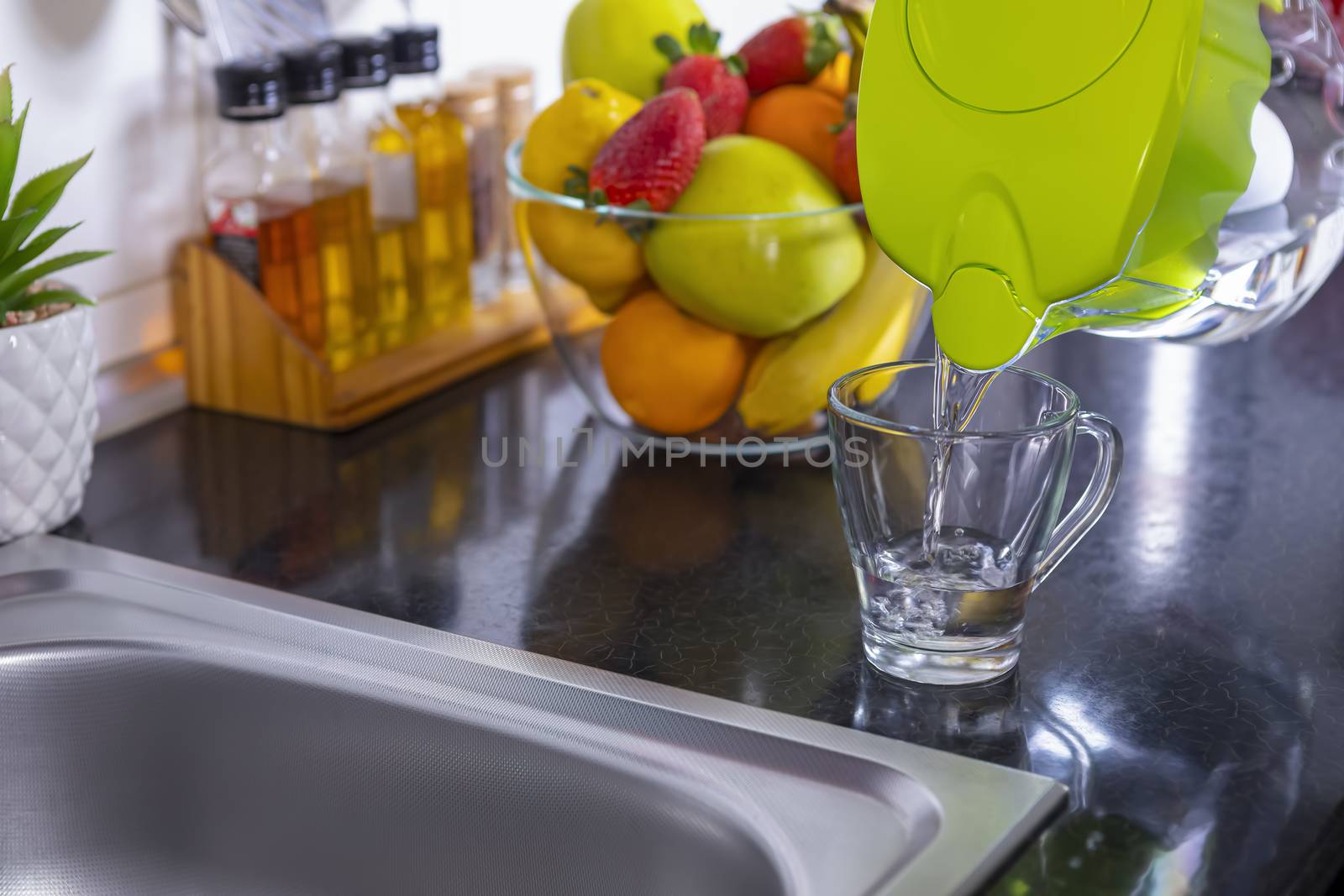 Pouring filtered water into glass from water filter jug in the kitchen. Purification and softening of drinking tap water. Closeup. Focus on glass.
