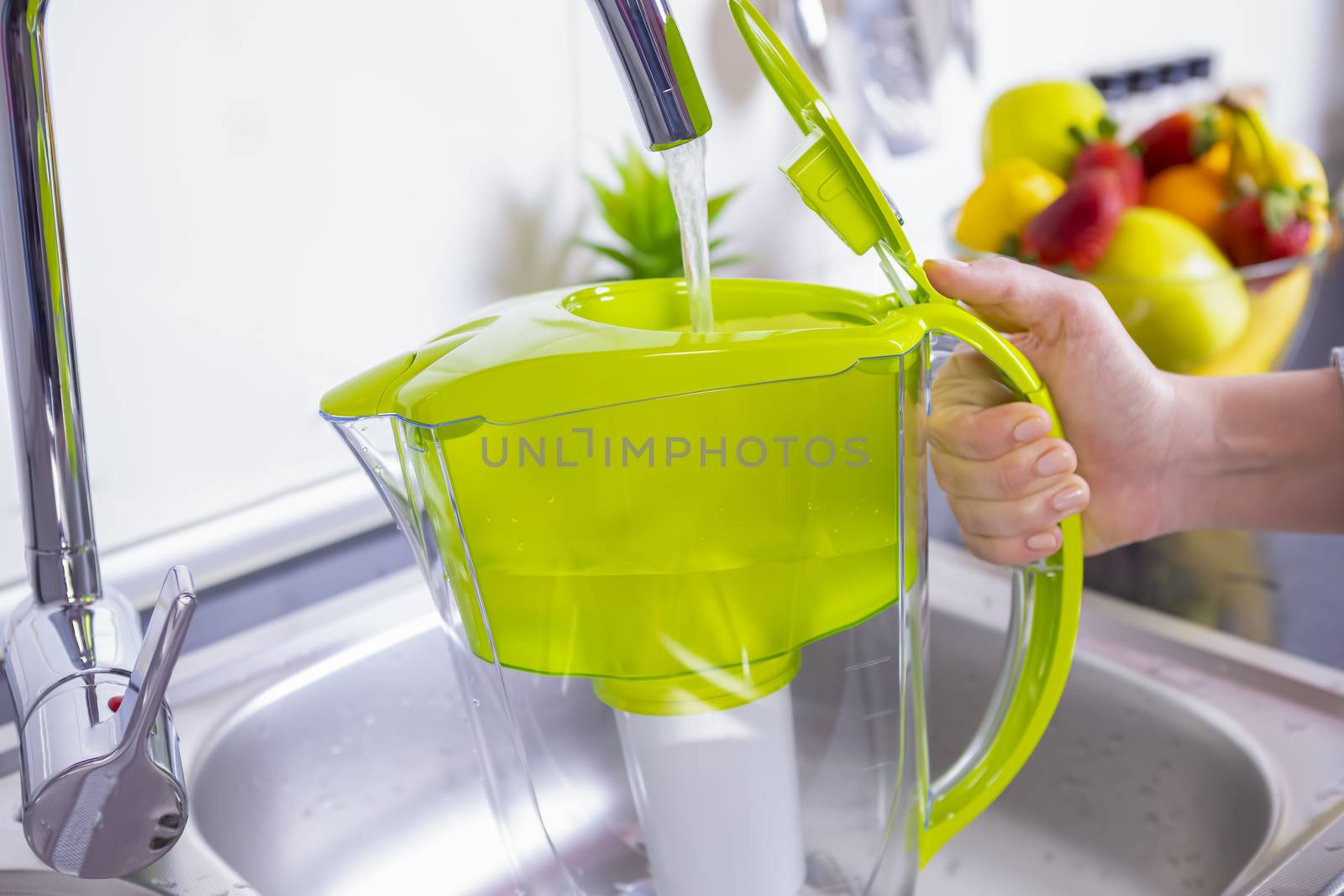 Woman filling water filter jug in the kitchen by manaemedia