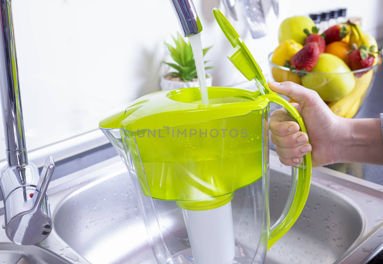 Woman filling water filter jug in the kitchen by manaemedia