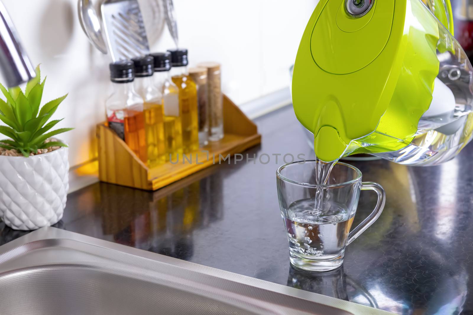 Pouring filtered water into glass from water filter jug in the kitchen. Purification and softening of drinking tap water. Closeup. Focus on glass.
