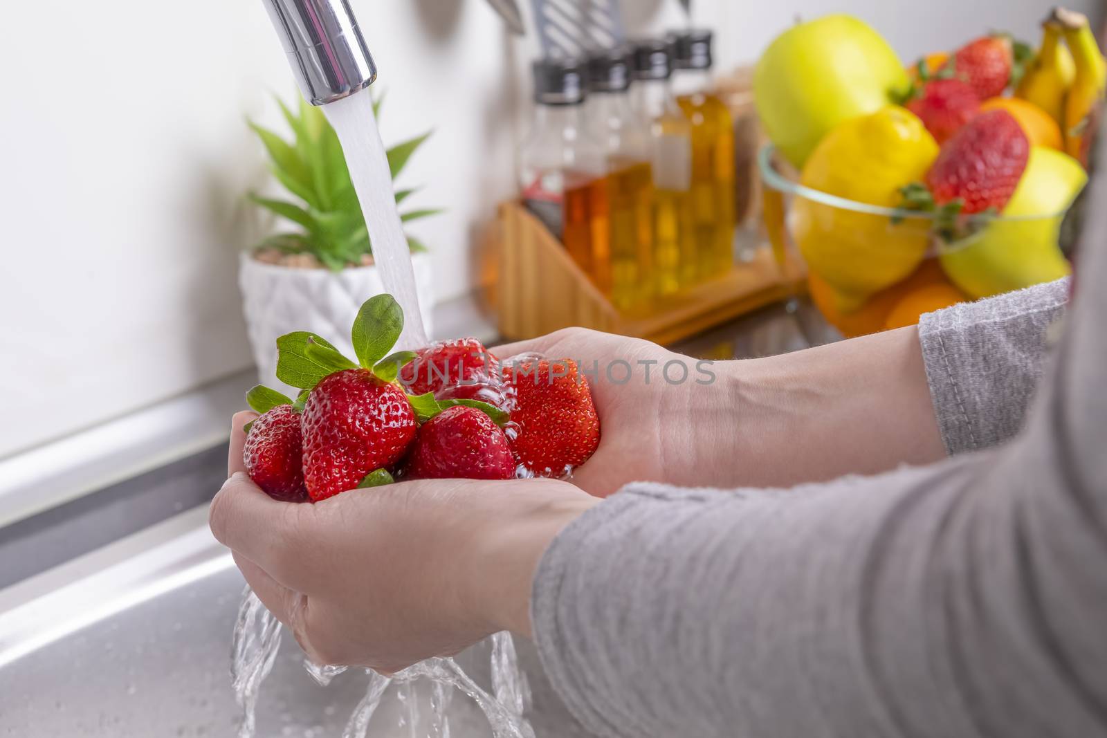 Woman washing strawberries in the kitchen by manaemedia