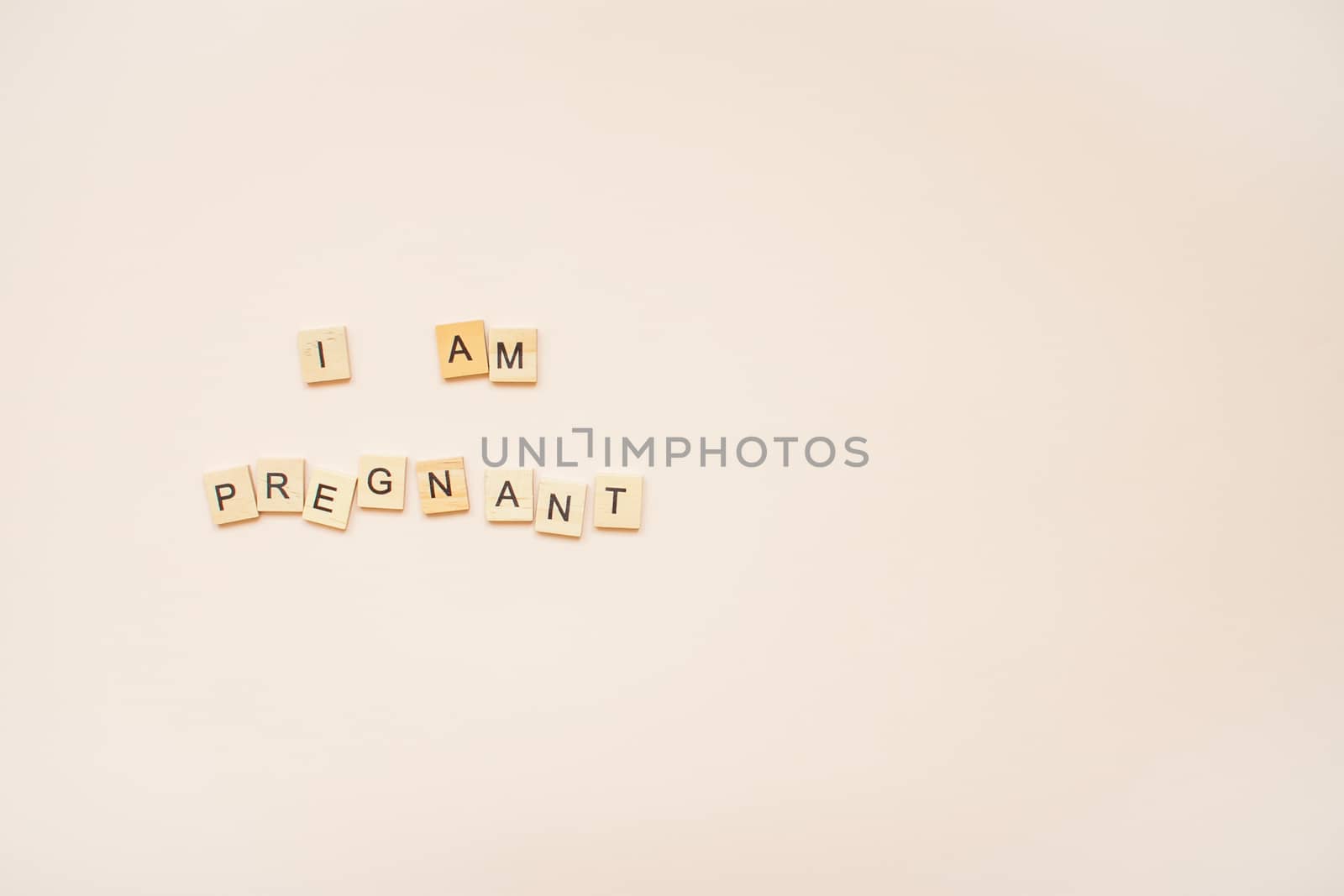 The inscription "I am pregnant" made of wooden blocks on a light pink background.