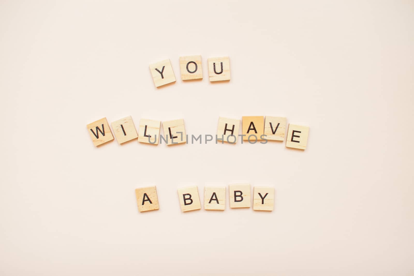 The inscription "you will have a baby" made of wooden blocks on a light pink background.