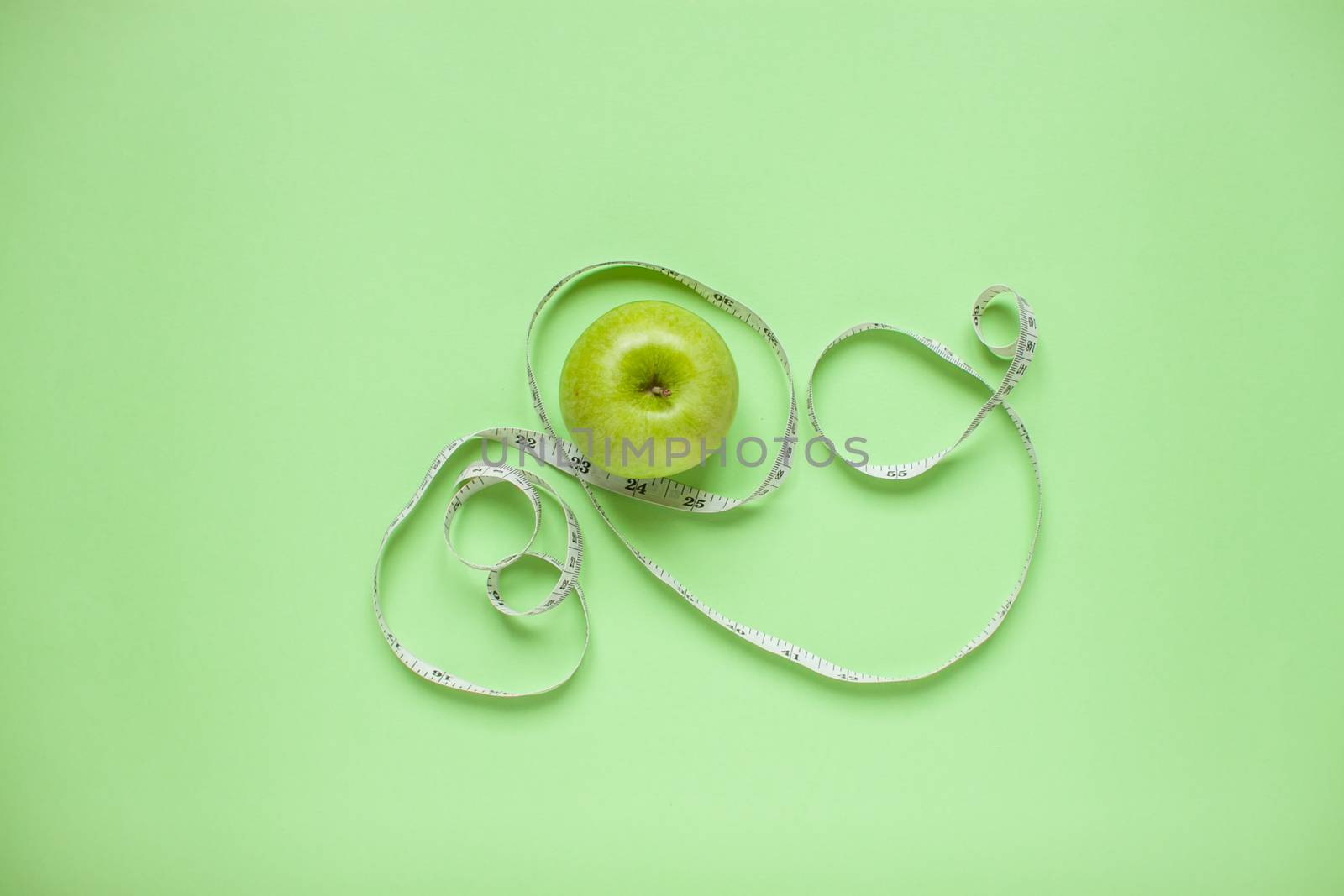 Diet and healthy eating concept. Top view of weightloss. Green apple and measuring tape. Green background by malyshkamju