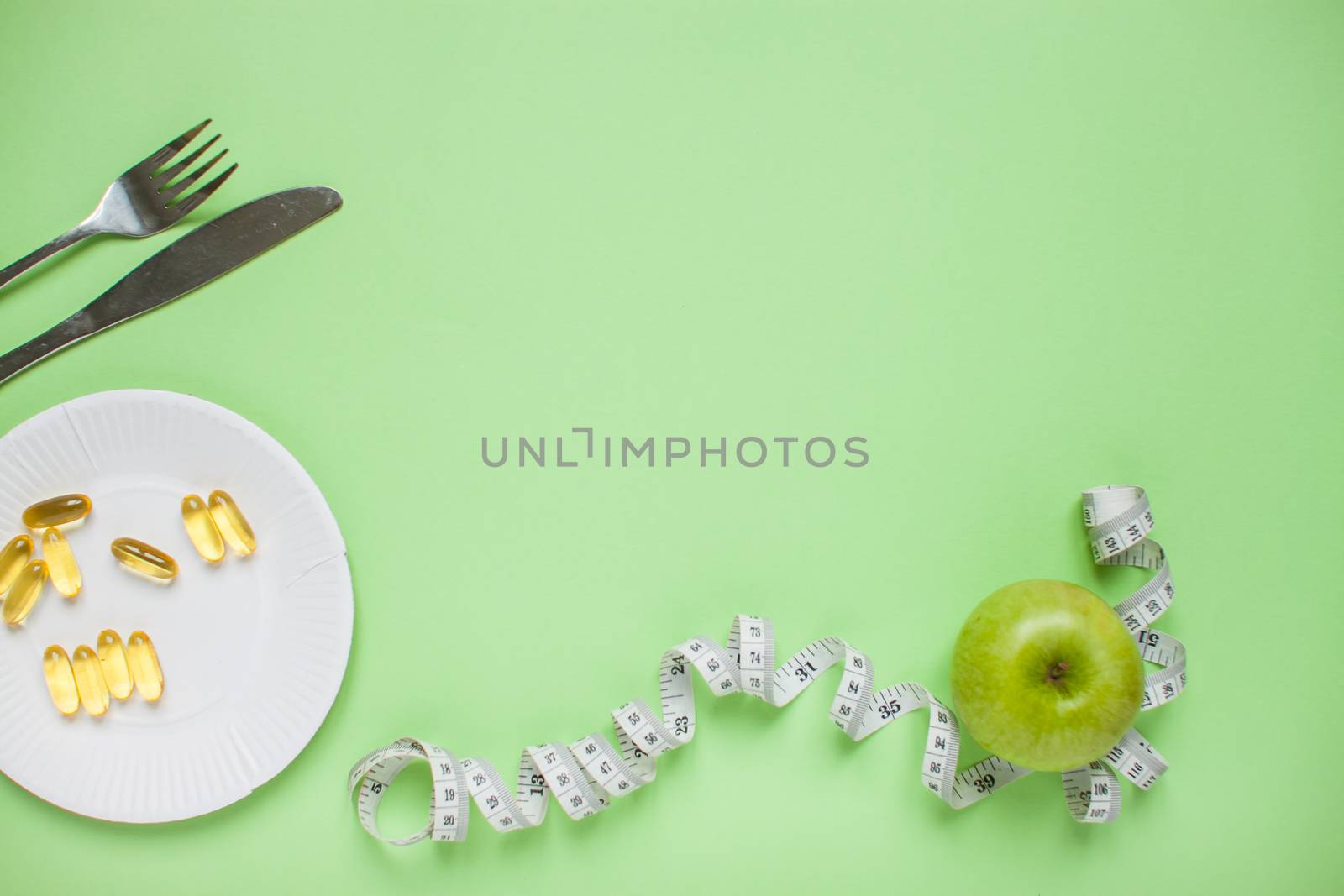Diet and healthy eating concept. Top view of weightloss. Green apple, measuring tape, knife with a fork, capsules, tablets. Green background
