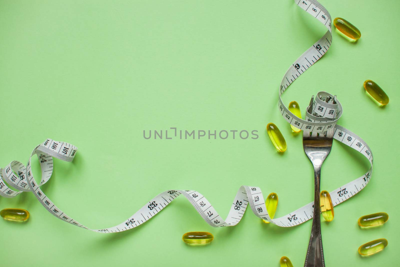 Diet and healthy eating concept. Top view of weightloss. Measuring tape on a fork. Capsules and diet pills. Green background by malyshkamju