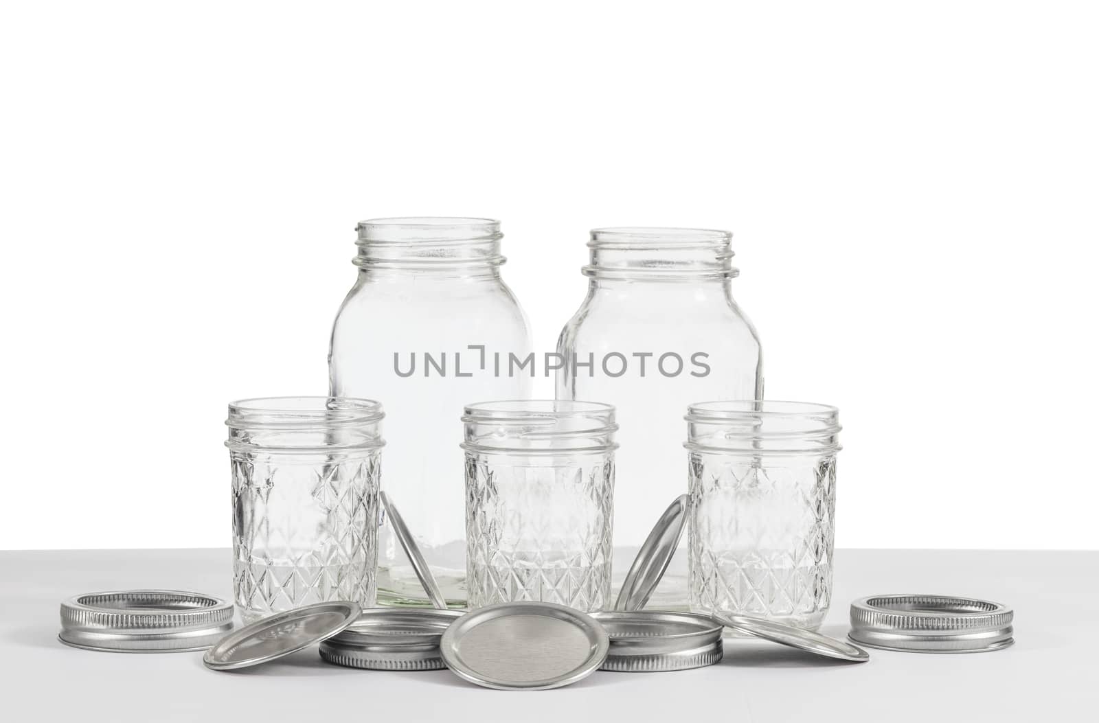 Horizontal shot of a group of old canning jars of two different sizes with rings and lids on a white background.