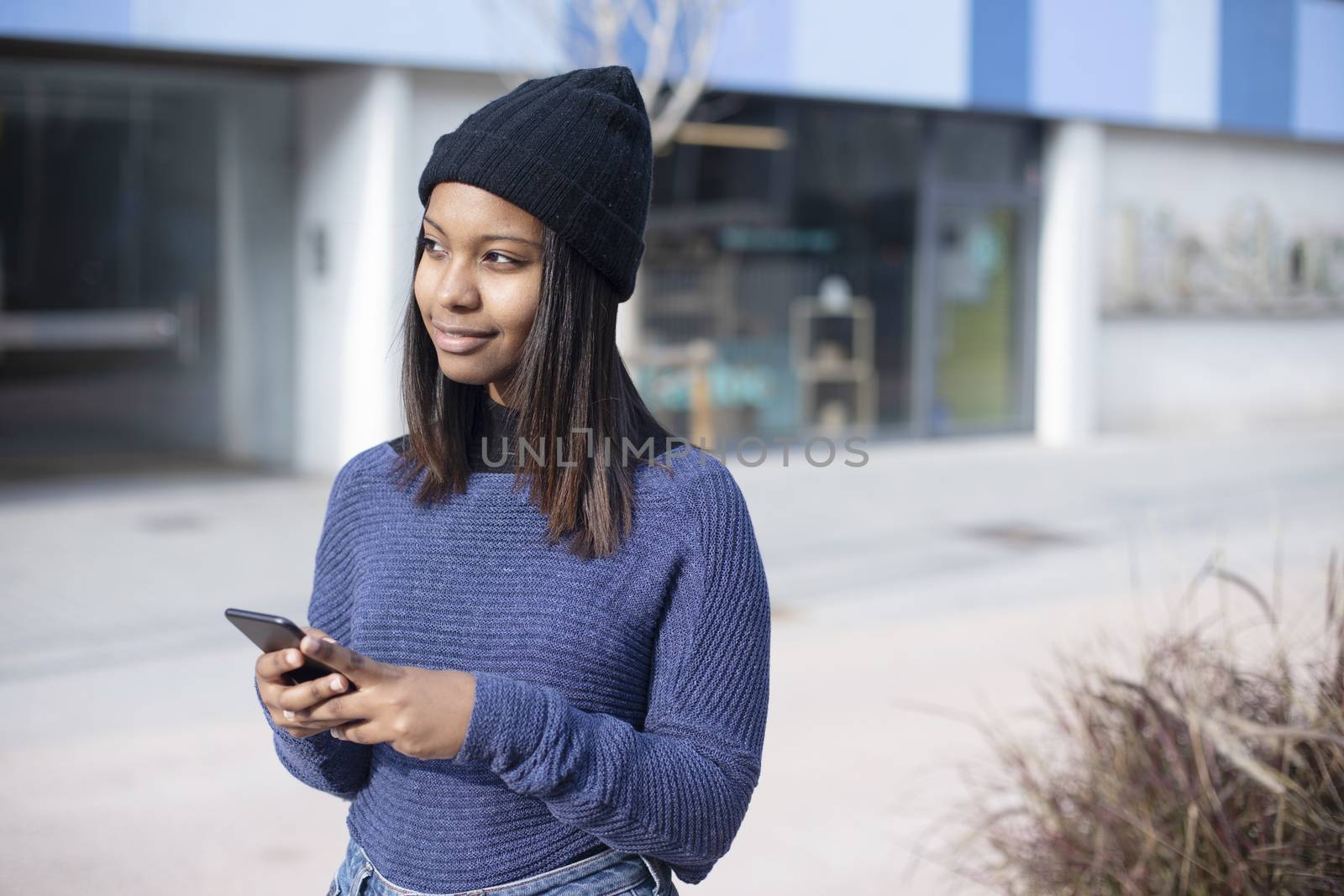Portrait of African American young woman wearing a wool cap standing on the street while using a mobile phone