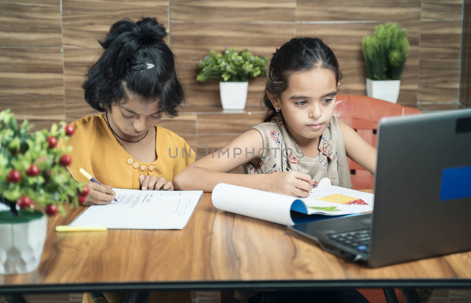 Two kids busy in writing by looking into the laptop during online or virtual class at home - concept of e-learning or distance learning or children lifestyle during coronavirus or covid-19 pandemic by lakshmiprasad.maski@gmai.com