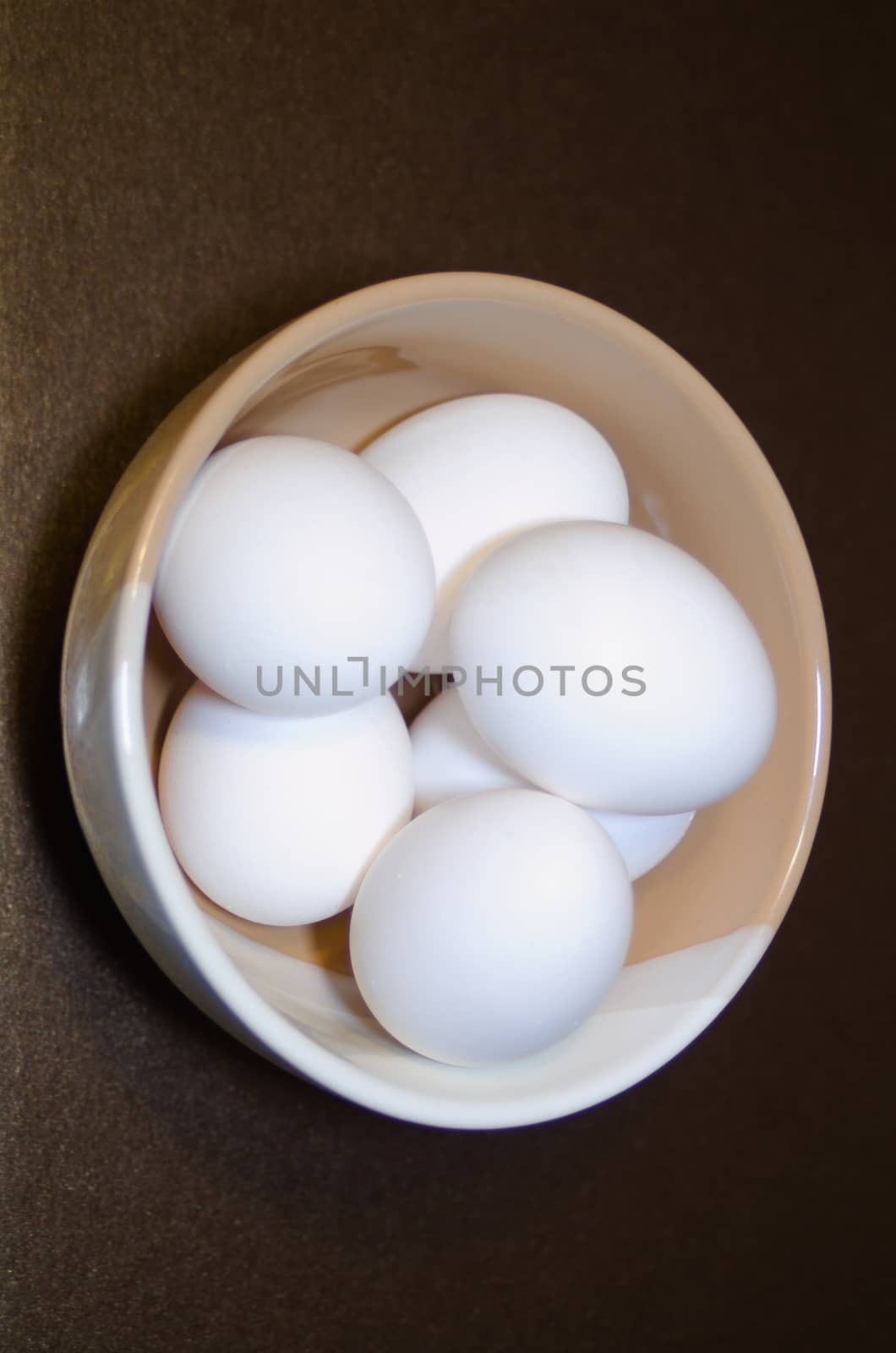 top view on white chicken eggs in a two-color bowl located on a dark background